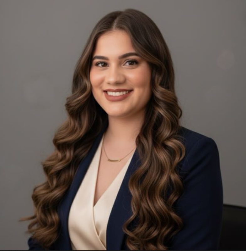 Retrato de Débora Ritielle, mulher de cabelos longos castanhos ondulados, sorrindo, vestindo blazer azul-marinho sobre blusa off-white.